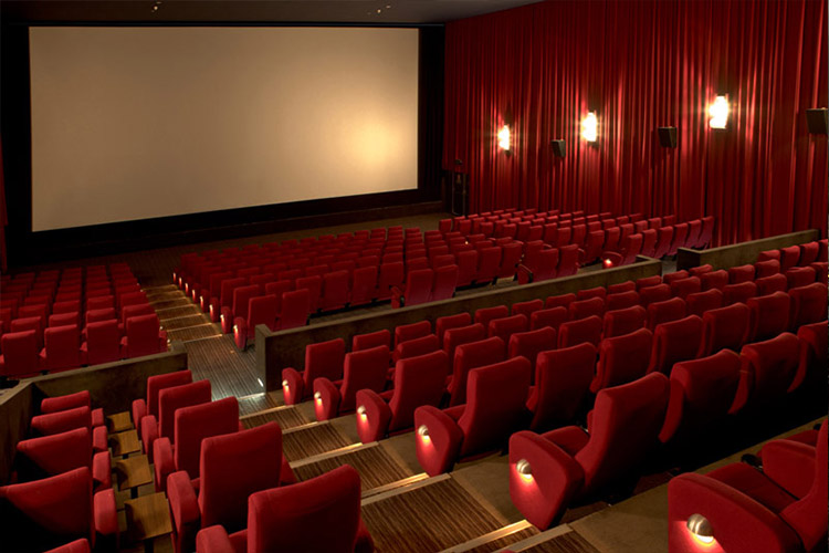 سینما خالی با صندلی قرمز و چراغ های زرد و پرده سفید